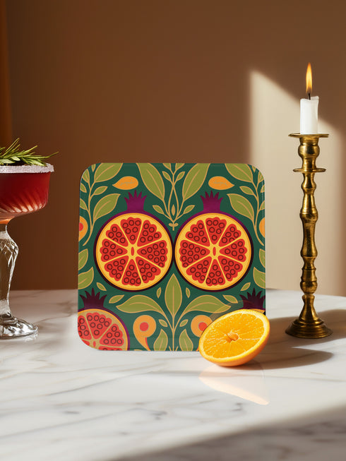 Set of four square drinking coasters featuring rich, dark green botanical illustration with highly detailed Pomegranate fruits and sliced cross-sections. The ornate pattern utilizes deep crimson, opulent gold, and ivory tones, strongly reflecting the stylized Art Nouveau period aesthetic and William Morris textile designs. Crafted from durable, resilient masonite hardboard, this luxury item features a protective high-gloss finish and a non-slip cork base.